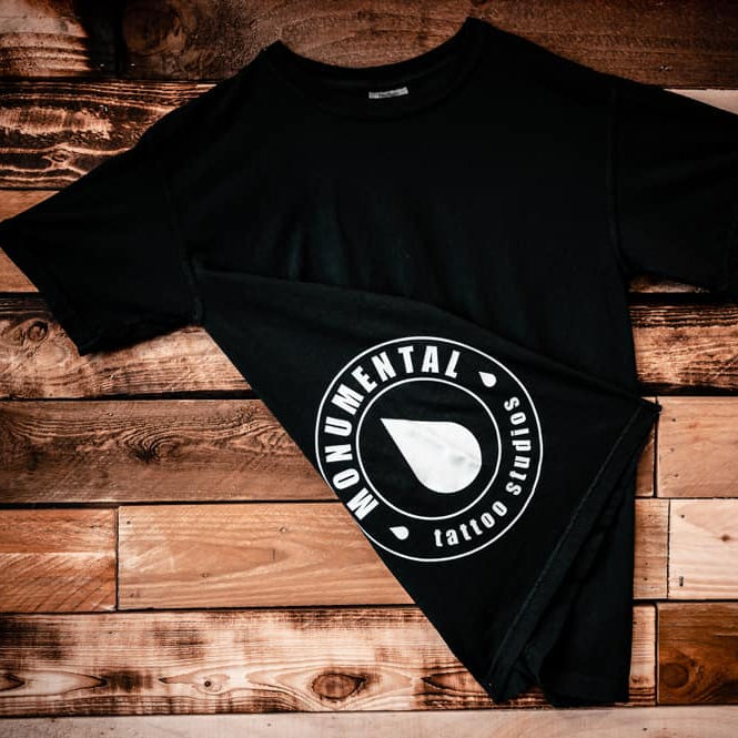 Black t-shirt with a monumental ink logo on a wooden surface
